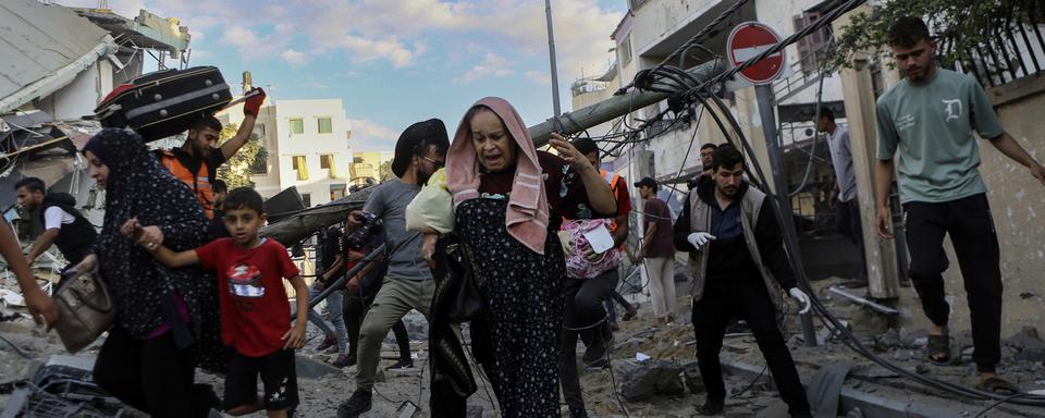 Des familles palestiniennes sortent précipitamment de leurs maisons après les frappes aériennes israéliennes visant leur quartier de la ville de Gaza, au centre de la bande de Gaza, le mardi 17 octobre 2023. [Keystone]