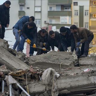 Des hommes turques enlèvent les débris d'un bâtiment effondré après les séismes qui ont frappé le pays. [AP Photo/Keystone - Khalil Hamra]