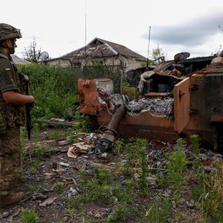 Un militaire ukrainien se tient à côté d'un véhicule de combat d'infanterie russe  détruit dans le village libéré de Blahodatne,près de la ligne de front dans la région de Donetsk, le 17 juin 2023. [Radio Free Europe/Reuters - Serhii Nuzhnenko]