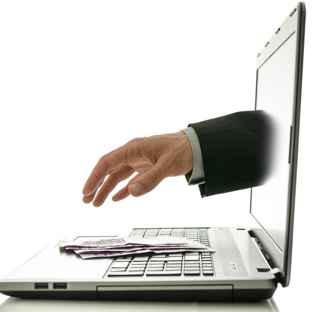 Une main sort d'un écran d'ordinateur pour attraper des billets de banque posés sur le clavier. [Depositphotos - Gajus-Images]