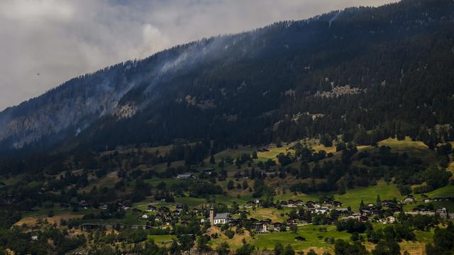 Un hélicoptère verse de l'eau pour éteindre la forêt au-dessus des communes de Bitsch et Ried-Moerel. [Keystone - Jean-Christophe Bott]