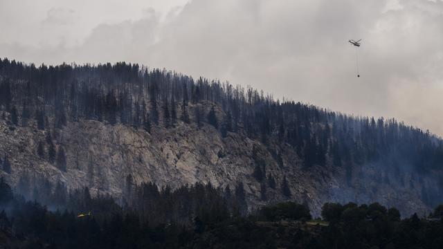 Un hélicoptère Super Puma verse de l'eau pour éteindre la forêt en feu au-dessus des communes de Bitsch. [Keystone - Jean-Christophe Bott]