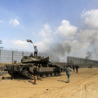 Des Palestiniens brandissent leur drapeau national et célèbrent la destruction d'un char israélien à la barrière de la bande de Gaza, à l'est de Khan Younis, dans le sud du pays, le samedi 7 octobre 2023. [Keystone - AP Photo/Yousef Masoud]
