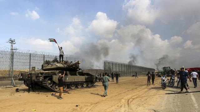 Des Palestiniens brandissent leur drapeau national et célèbrent la destruction d'un char israélien à la barrière de la bande de Gaza, à l'est de Khan Younis, dans le sud du pays, le samedi 7 octobre 2023. [Keystone - AP Photo/Yousef Masoud]