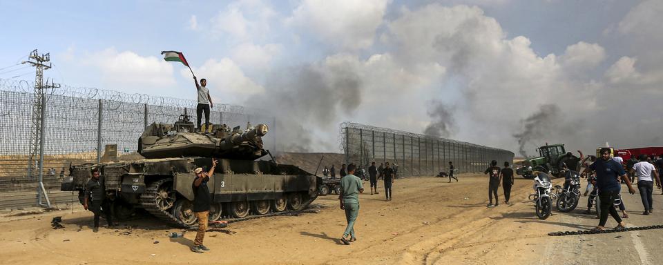 Des Palestiniens brandissent leur drapeau national et célèbrent la destruction d'un char israélien à la barrière de la bande de Gaza, à l'est de Khan Younis, dans le sud du pays, le samedi 7 octobre 2023. [Keystone - AP Photo/Yousef Masoud]