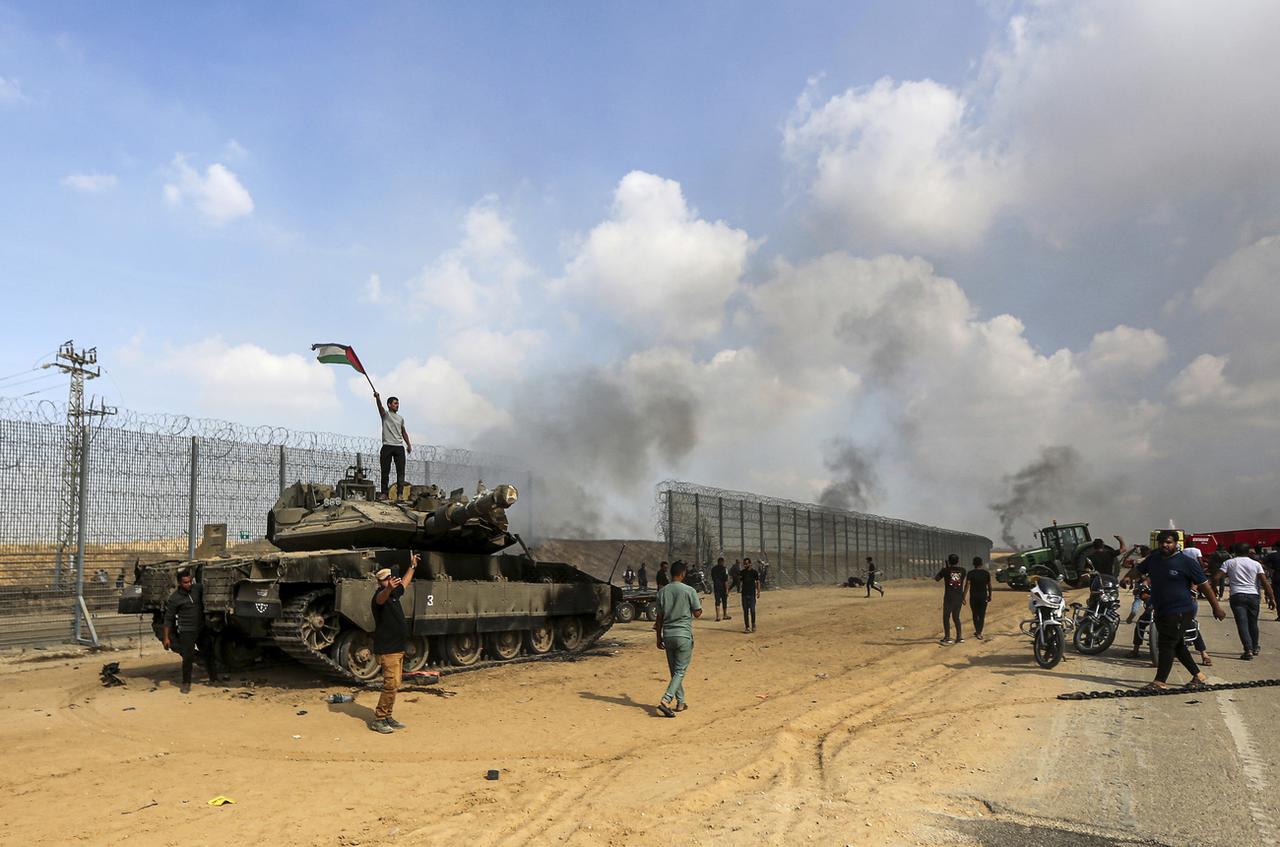 Des Palestiniens brandissent leur drapeau national et célèbrent la destruction d'un char israélien à la barrière de la bande de Gaza, à l'est de Khan Younis, dans le sud du pays, le samedi 7 octobre 2023. [Keystone - AP Photo/Yousef Masoud]