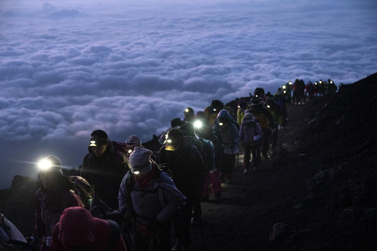 Un groupe de randonneurs gravit les pentes du Mont Fuji avant le lever du soleil, le 27 août 2019. [Keystone - Jae C. Hong/AP Photo]