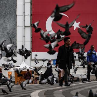 Des personnes se baladent dans une ruelle de Bursa, en face d'un drapeau d'Erdogan et du drapeau national turc. [Keystone/EPA - Erdem Sahin]