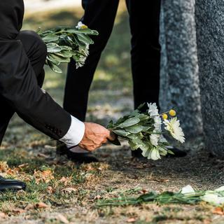 Un homme âgé dépose des fleurs près d'une pierre tombale. [Depositphotos - Andrew Lozovyi]
