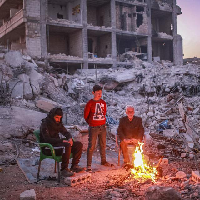 Dimanche 19 février: une famille réunie au bord du feu devant un immeuble détruit à Alep, en Syrie. [Keystone - Muhammed Said/Anadolu Agency]