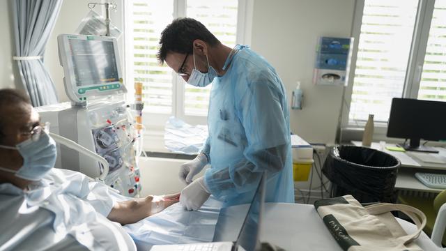 Un infirmier place une aiguille dans le bras d'un patient pour le connecter à l'appareil de dialyse et nettoyer son sang, lundi 22 août 2022, dans le service de néphrologie du Centre hospitalier universitaire vaudois (CHUV) à Lausanne (image d'illustration). [KEYSTONE - Gaetan Bally]
