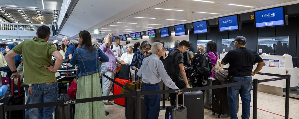 Des passagers attendent avec leurs bagages devant les guichets d'embarquement de l'aéroport de Genève. [Keystone - Martial Trezzini]