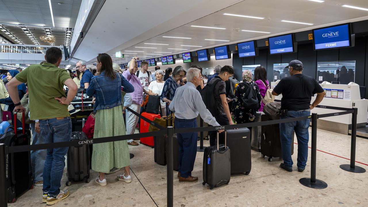 Des passagers attendent avec leurs bagages devant les guichets d'embarquement de l'aéroport de Genève. [Keystone - Martial Trezzini]