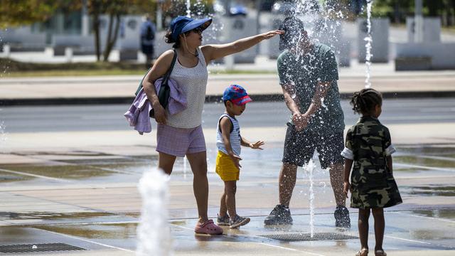 Des touristes profitent des jets d'eau pour se rafraîchir a la fontaine de la Place des Nations, à Genève le 18 aout 2023. [Keystone - Martial Trezzini]