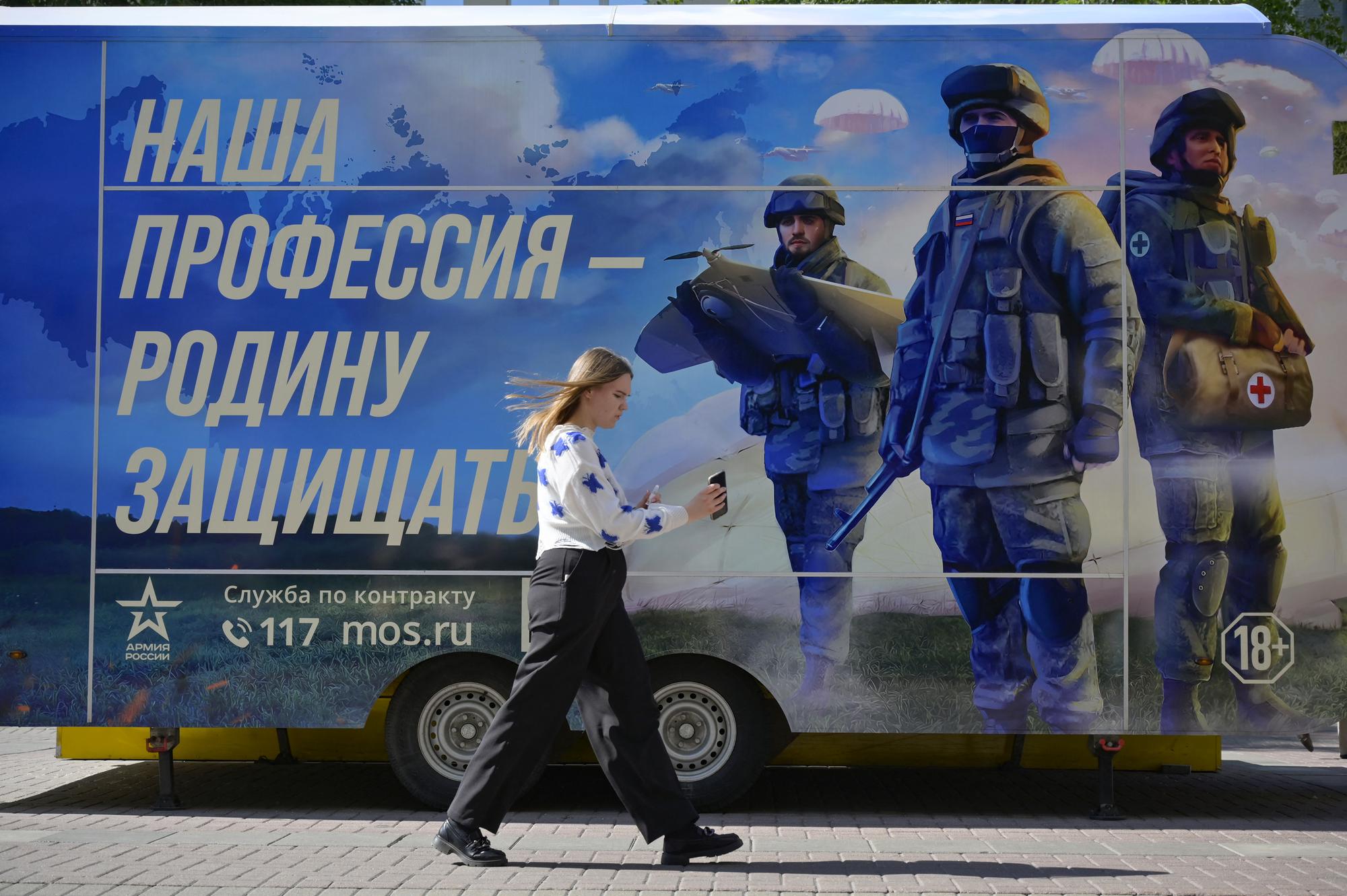 Une femme passe devant un point de recrutement mobile du service militaire contractuel à Moscou, le 14 juin 2023. Le slogan est le suivant: "Notre profession est de défendre la patrie". [AFP - NATALIA KOLESNIKOVA]