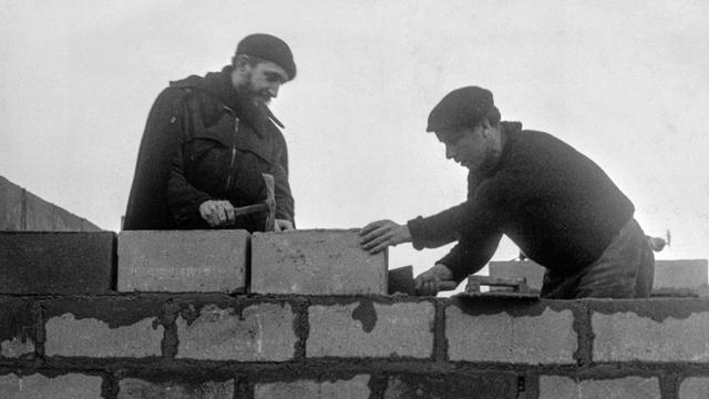 Prêtre catholique et fondateur de l'association caritative Emmaüs, l'abbé Pierre, à gauche, aide un maçon dans la construction d'abris temporaires conçus par l'architecte François Spoerry dans la commune française du Plessis-Trévise le 11 mars 1954. [Keystone/AP - Photopress-archiv/Str]