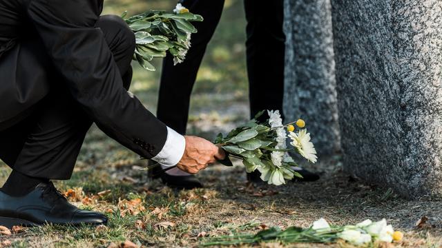 Un homme âgé dépose des fleurs près d'une pierre tombale. [Depositphotos - Andrew Lozovyi]