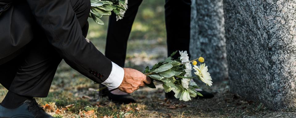 Un homme âgé dépose des fleurs près d'une pierre tombale. [Depositphotos - Andrew Lozovyi]