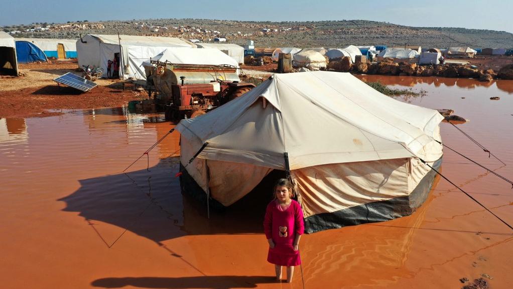 Une jeune fille debout devant une tente dans un camp inondé en Syrie, abritant des Syriens déplacés suite aux fortes pluies de la veille, le 17 décembre 2020. [AFP - Omar Haj Kadour]