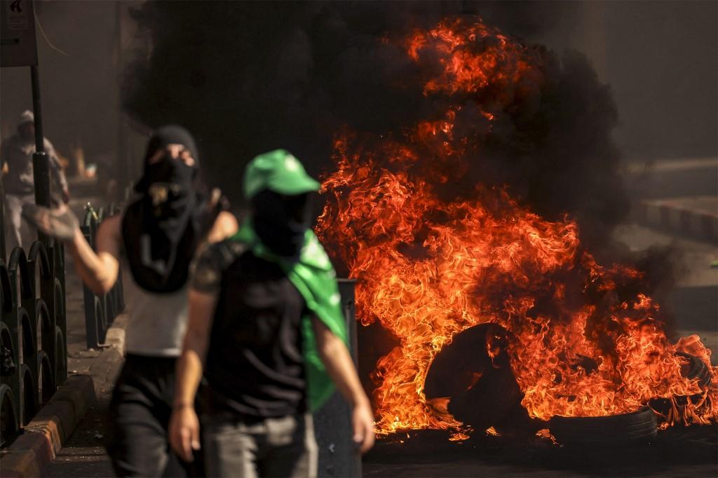 Des manifestants palestiniens masqués marchent près de pneus enflammés lors d'affrontements avec les forces israéliennes à la suite d'un rassemblement de solidarité avec Gaza par des partisans des mouvements Fatah et Hamas, dans la ville d'Hébron en Cisjordanie occupée, le 13 octobre 2023. [AFP - HAZEM BADER]