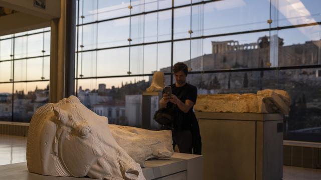 Un homme prend une photo du char à quatre chevaux de Séléné au musée de l'Acropole avec l'ancien temple du Parthénon en arrière-plan lors d'une cérémonie pour le rapatriement de trois fragments de sculpture à Athènes, le 24 mars 2023. [keysttone - Petros Giannakouris]