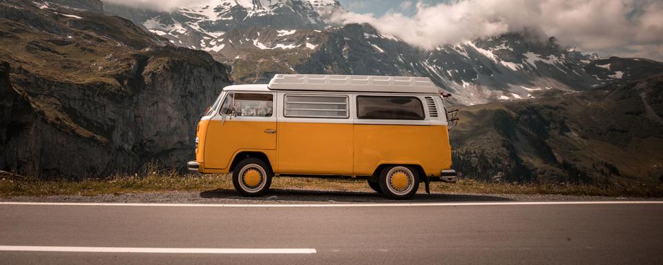 Un van garé sur le bord de la route devant des montagnes. [Unsplash - Kevin Schmid]