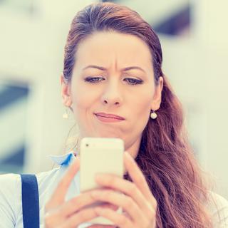 Une femme regarde son téléphone portable d'un air dubitatif. [Depositphotos - Slphotography]