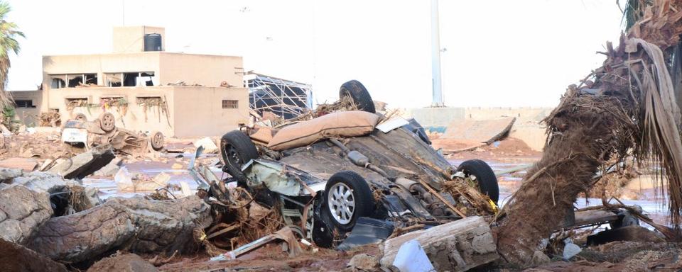 Un véhicule endommagé est coincé dans des débris après les inondations causées par la tempête Daniel à Derna, en Libye le 12 septembre 2023. [AFP - Abdullah Mohammed Bonja / Anadolu Agency]