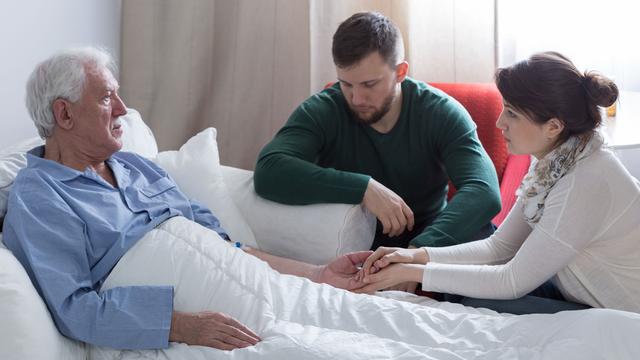 Un homme dans un lit d'hôpital accompagné de deux personnes plus jeunes. [Depositphotos - photographee.eu]