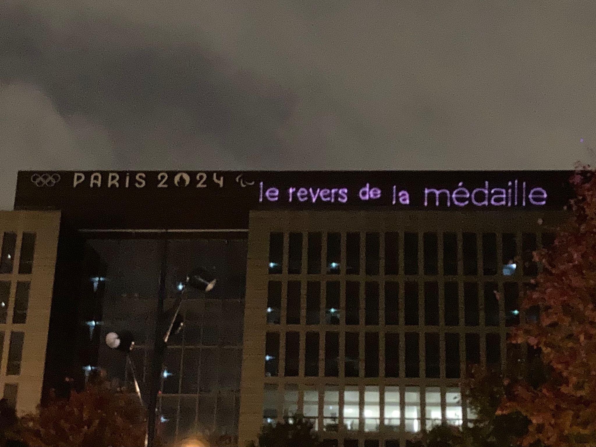 Le message "Le revers de la médaille" projeté par un collectif militant sur le bâtiment du Comité d'organisation des Jeux olympiques fin octobre. [Utopia 56]