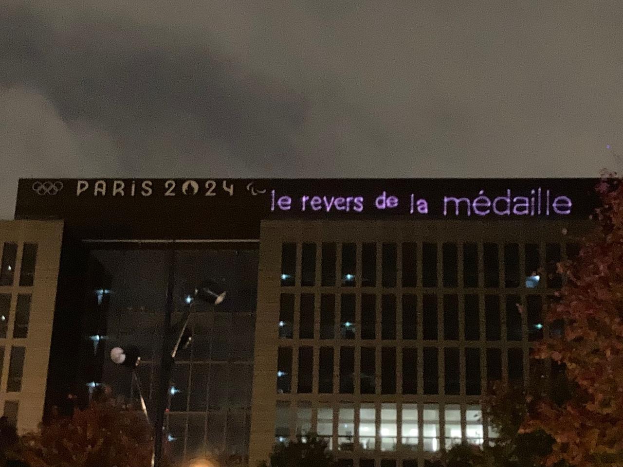 Le message "Le revers de la médaille" projeté par un collectif militant sur le bâtiment du Comité d'organisation des Jeux olympiques fin octobre. [Utopia 56]