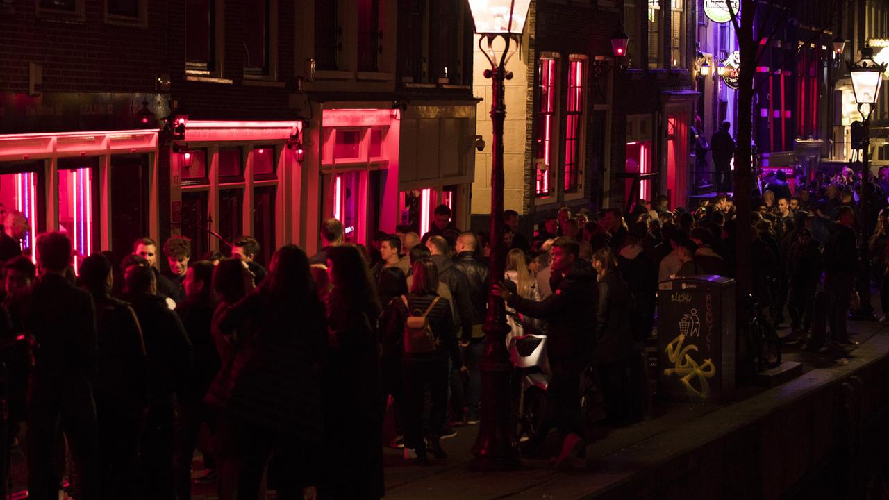 Des touristes se pressent sur les quais du quartier rouge d'Amsterdam, devant les vitrines des prostituées et les peep shows. [AP/Keystone - Peter Dejong]