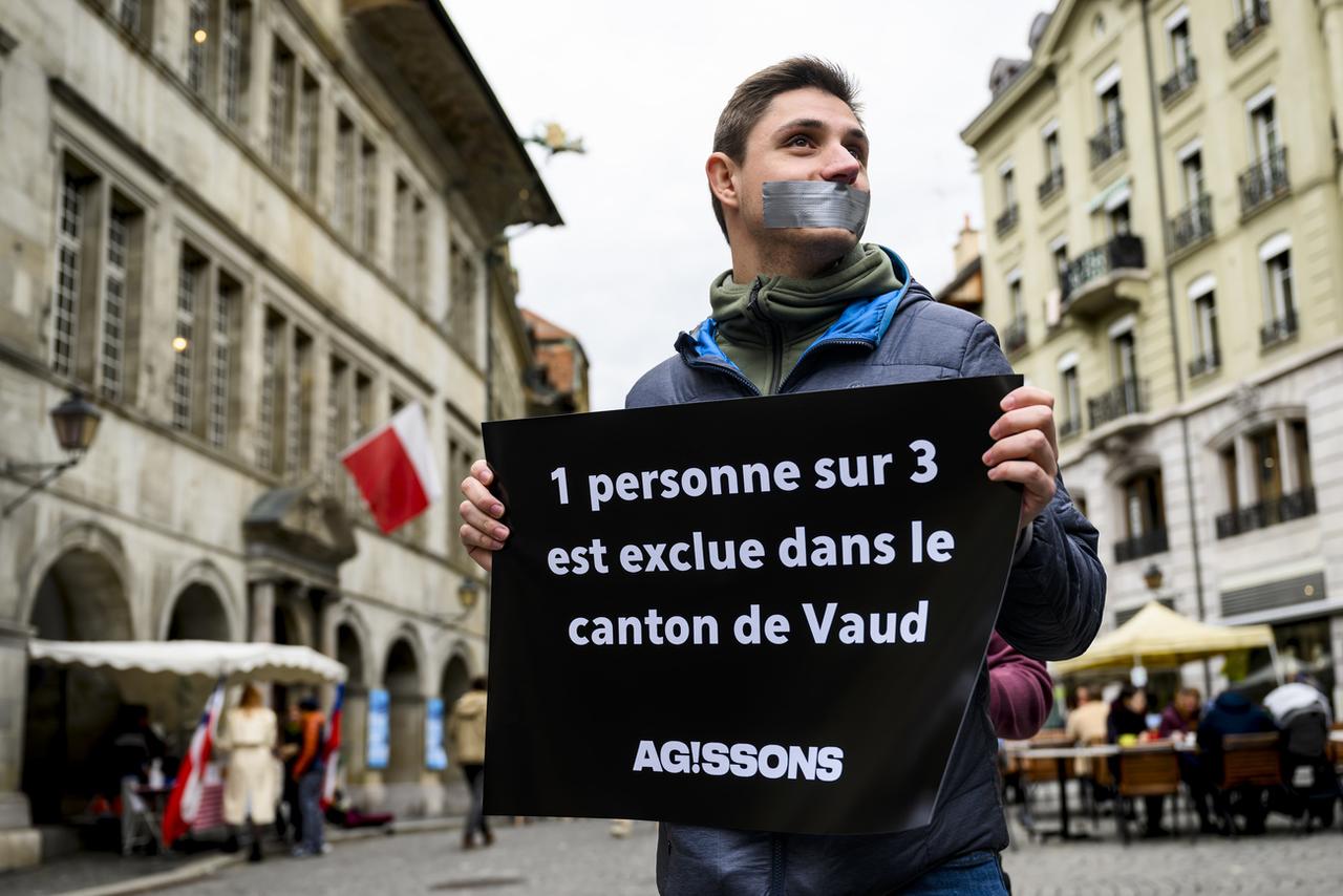 Un membre du mouvement citoyen Ag!ssons tient une pancarte indiquant qu'"1 personne sur 3 est exclue dans le canton de Vaud" lors du lancement de la campagne pour deux initiatives populaires vaudoises sur la démocratie, à Lausanne. [Keystone - Jean-Christophe Bott]