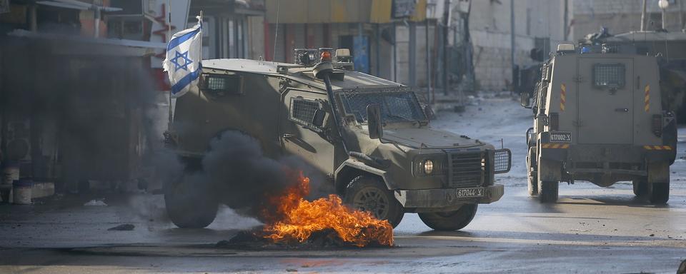 Des débris en feu bloquent partiellement une route alors que les forces de défense israéliennes mènent un raid pour le deuxième jour dans un camp de réfugiés près de la ville de Jénine en Cisjordanie, le 13 décembre 2023. [KEYSTONE - ALAA BADARNEH]