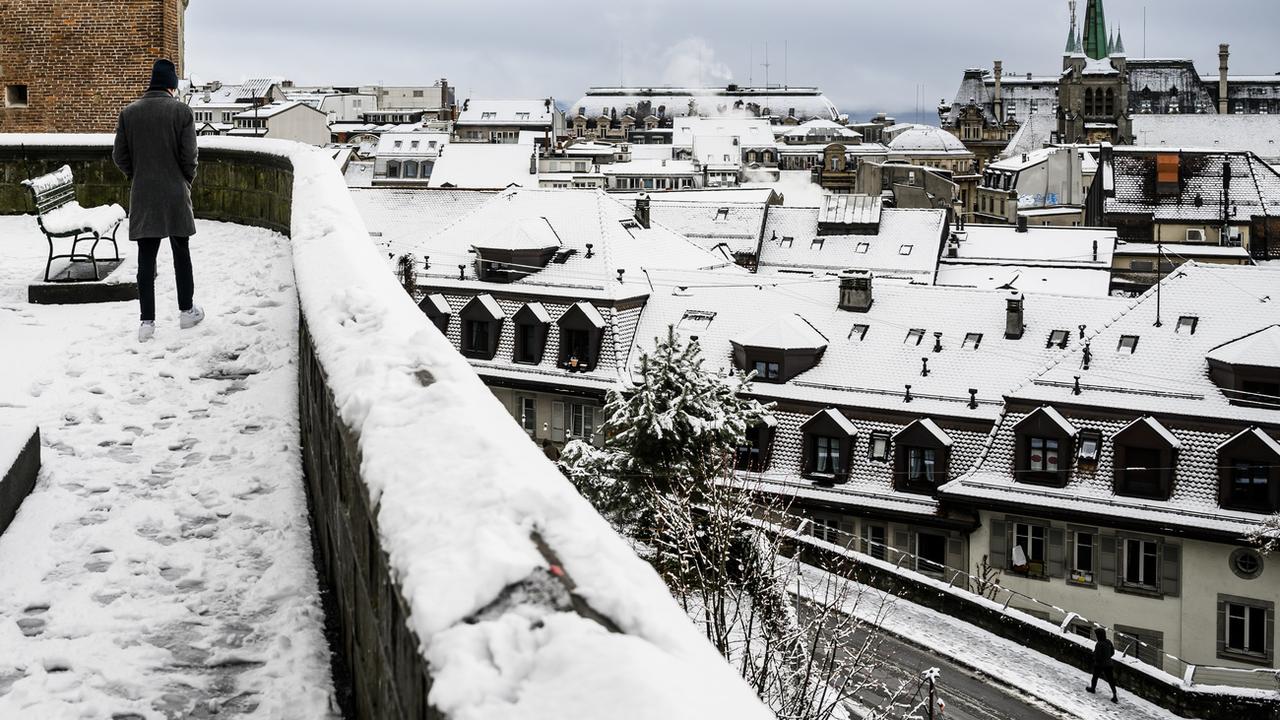 Des personnes marchent dans la neige qui recouvre les rues du centre-ville de Lausanne. [Keystone - Jean-Christophe Bott]