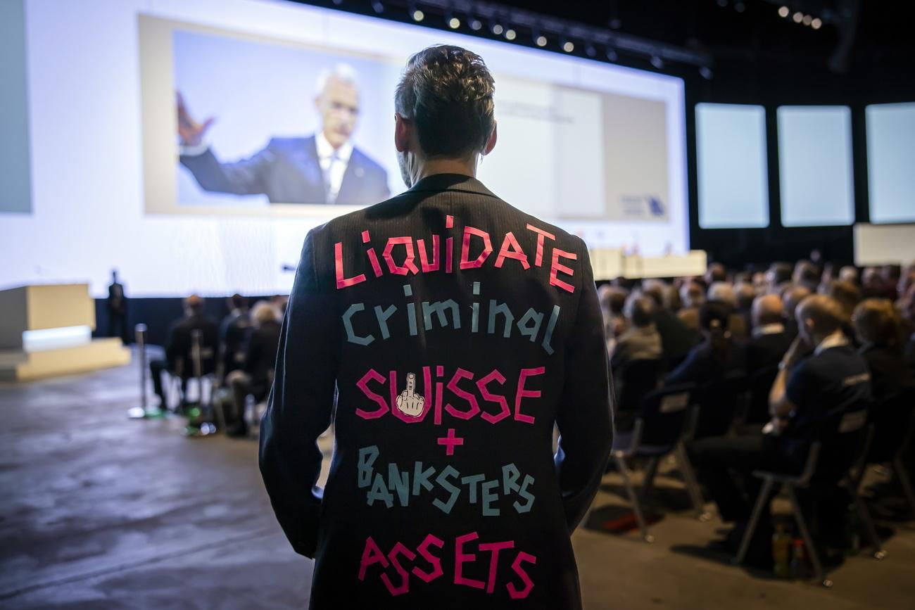 Un homme porte un costume avec l'inscription "Liquidate Criminal Suisse + Banksters Assets" alors que le président de Credit Suisse Axel P. Lehmann s'exprime lors de l'assemblée annuelle des actionnaires du groupe bancaire à Zurich. [Keystone - Michael Buholzer]