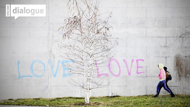 Deux personnes passent devant un mur sur lequel le mot "Love" est tagué deux fois. [Keystone - Michael Buholzer]