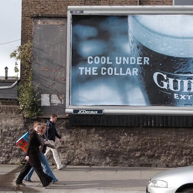 Un groupe de jeunes passe devant une publicité une célèbre bière irlandaise, à Dublin. [Keystone/AP Photo - John Cogill]