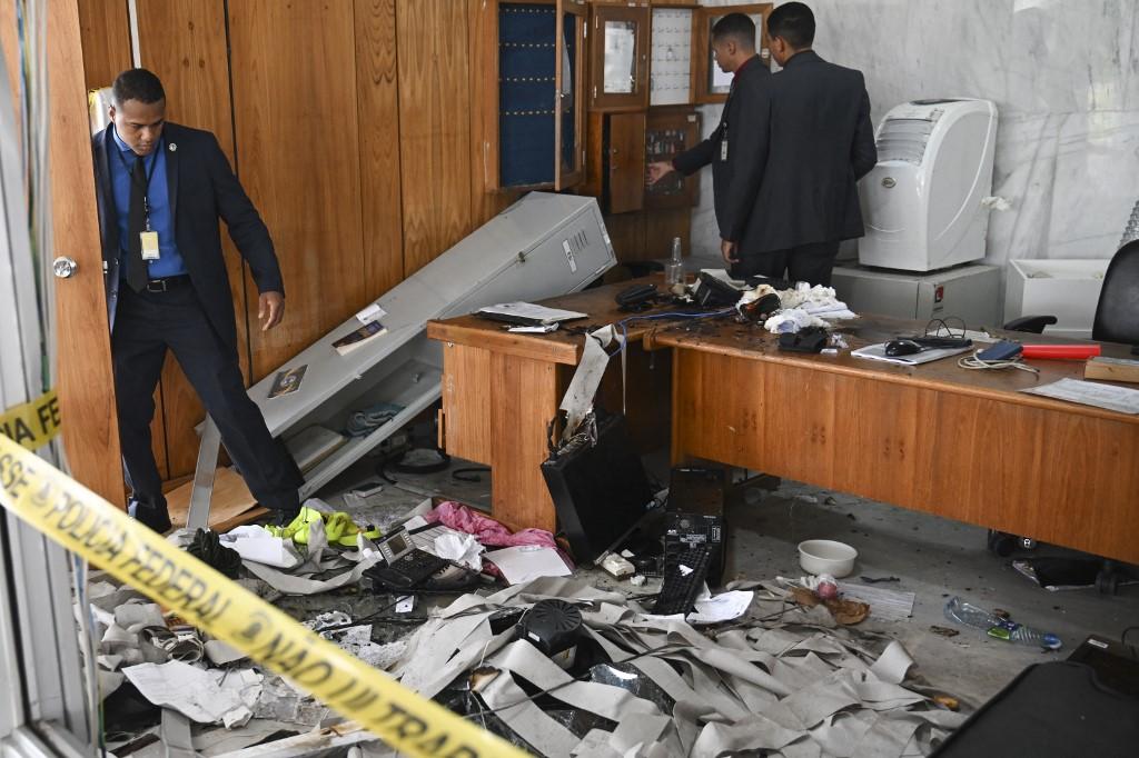 Des membres de la sécurité du Palais présidentiel constatent les dégâts le 9 janvier 2023. [AFP - Carl de Souza]