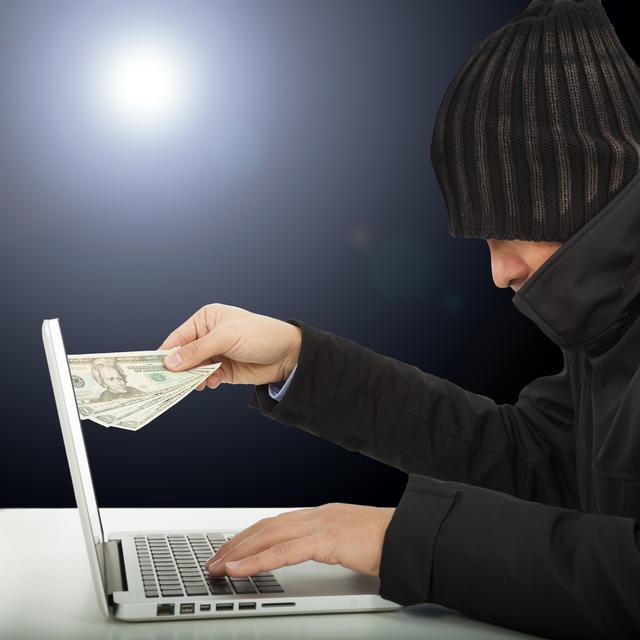Un arnaqueur en ligne retire de l'argent de son ordinateur. [Depositphotos - Tom Wang]