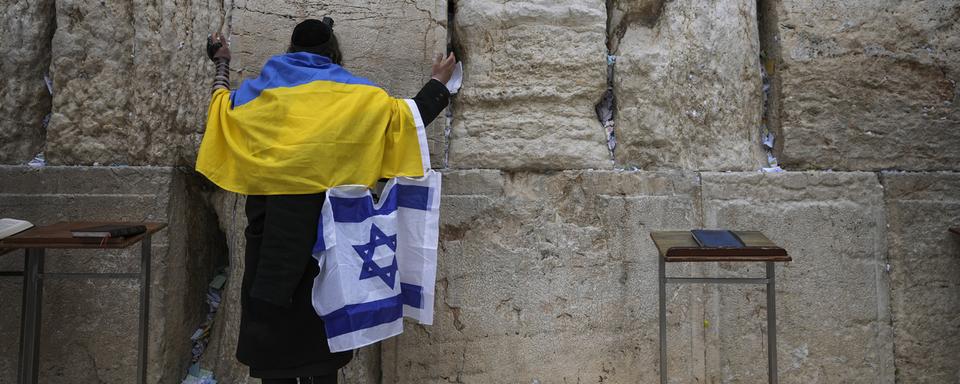 Un juif ultra-orthodoxe enveloppé dans des drapeaux nationaux ukrainien et israélien prie au Mur occidental, le site le plus sacré où les juifs peuvent prier dans la vieille ville de Jérusalem, le vendredi 4 mars 2022. [Keystone - AP Photo/Mahmoud Illean]