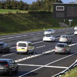 Une voiture attend a un feu rouge sur la rampe de dosage alors que des voitures circulent sur sur l'autoroute A1 entre Yverdon et Lausanne. [Keystone]