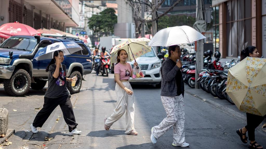 Des habitants de Bangkok se protègent du soleil avec des parapluies en pleine canicule, le 20 avril 2023. [AFP - Jack Taylor]