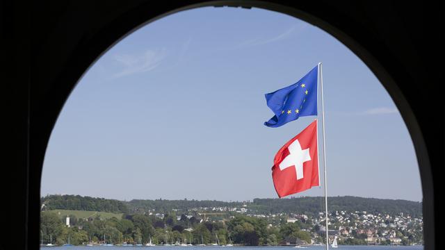 Un drapeau européen et un drapeau suisse flottent dans le vent au bord du lac de Zurich. [Keystone - Gaëtan Bally]