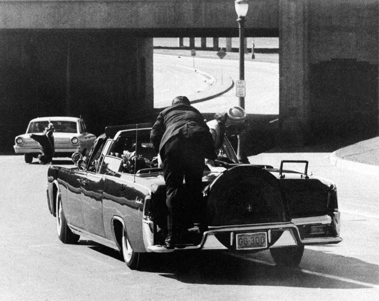 Jacqueline Kennedy se penche sur son époux, dont le corps a glissé, et l'agent du Secret Service Clinton Hill saute à l'arrière de la Lincoln bleu. [Keystone - AP Photo/Ike Altgens]