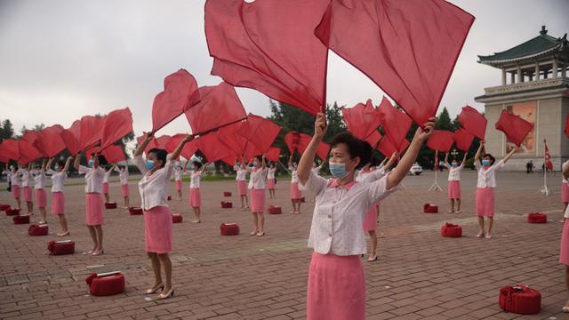 Des membres du Comité du district central de la ville de Pyongyang de l'Union des femmes socialistes de Corée exécutent une routine de propagande en agitant un drapeau aux heures de pointe, sur la place du Grand Théâtre, le 19 juin 2021. [AFP]