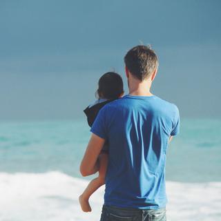 Un parent et son enfant se tiennent de dos, face à la mer. [Unsplash - Steven Van Loy]