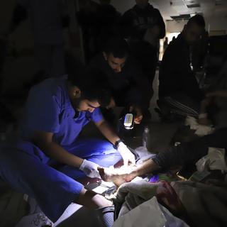 Des infirmiers et médecins palestiniens soignant une personne à l'aide de lampes-torches. [Keystone/AP Photo - Ahmed Alarini]