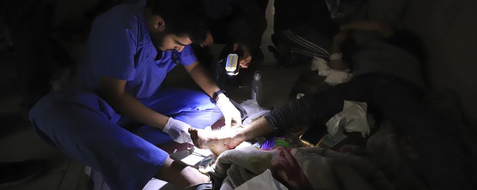 Des infirmiers et médecins palestiniens soignant une personne à l'aide de lampes-torches. [Keystone/AP Photo - Ahmed Alarini]