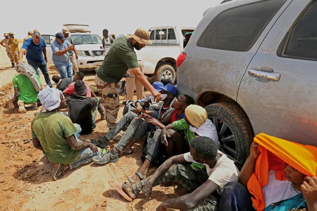 Des migrants d'origine africaine, qui auraient été abandonnés par les autorités tunisiennes, reçoivent de l'eau à leur arrivée dans une zone inhabitée près d'Al-Assah, à la frontière entre la Libye et la Tunisie, le 30 juillet 2023. [AFP - MAHMUD TURKIA]